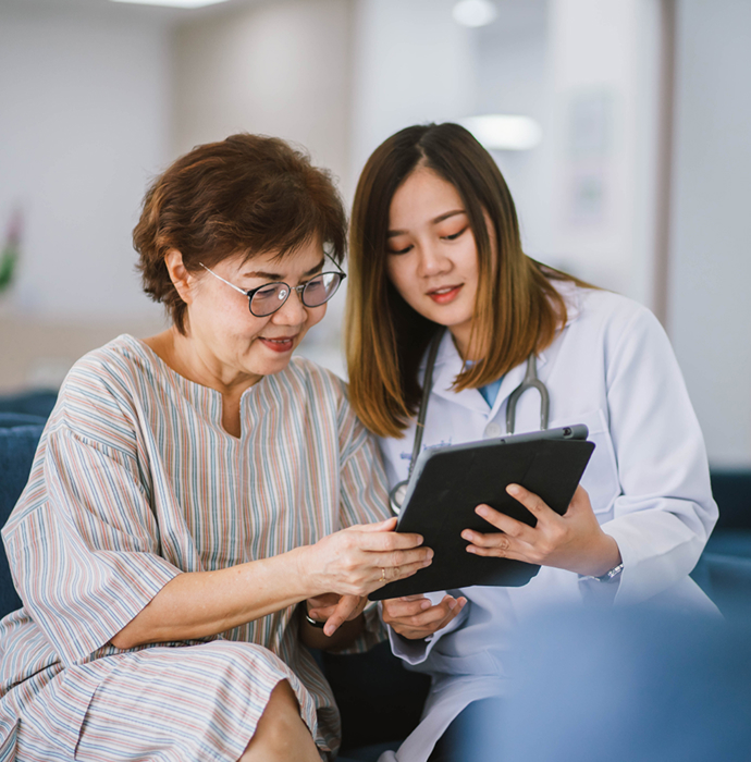 A doctor sitting with an elderly woman, attentively looking at a tablet, showcasing a caring and professional interaction.